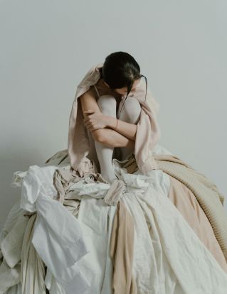 Contemplative woman sitting in a pile of clothes, embodying themes of solitude and introspection.