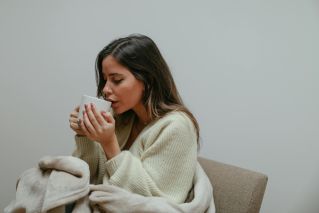 Woman wrapped in a blanket, sipping from a mug, enjoying a relaxing moment indoors.