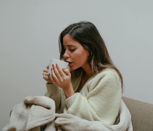 Woman wrapped in a blanket, sipping from a mug, enjoying a relaxing moment indoors.